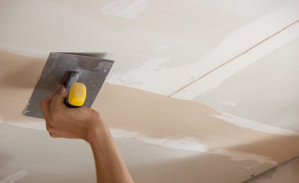 A man puts putty on a plasterboard ceiling. Putty for the joints of plasterboard sheets