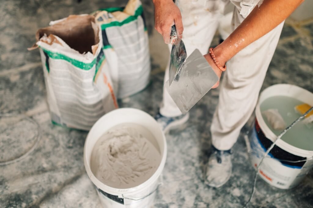 Builder's hands holding trowel and spatula and preparing for skim coating walls.