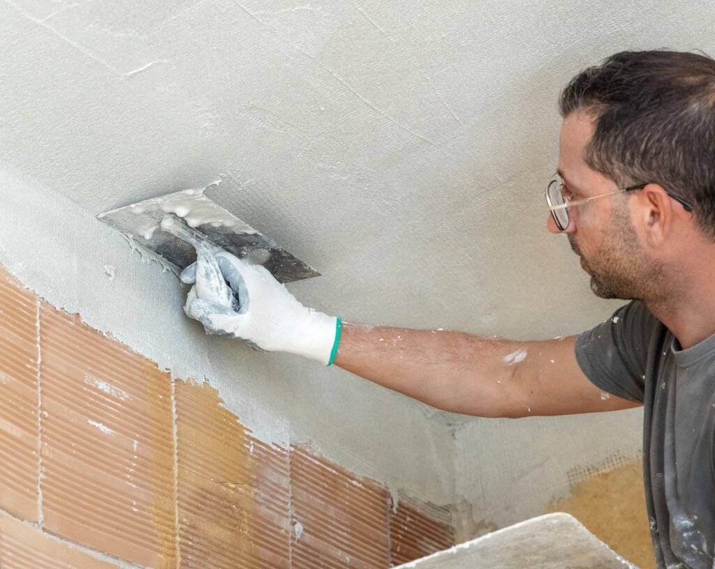 Kirli eldivenler ve gri gömlek giymiş ustanın tavan üzerinde metal sıva ile sıva yapması