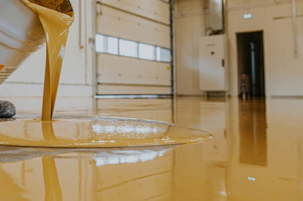 Worker, coating floor with self-leveling epoxy resin in industrial workshop.